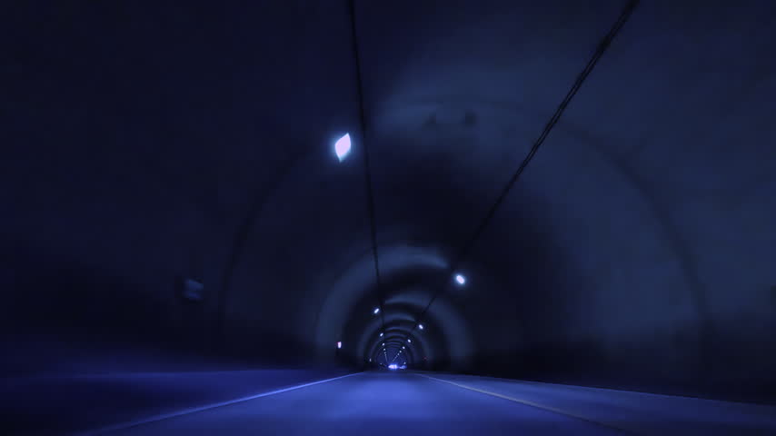 The interior of a quiet tunnel with a line of lights stretching through the darkness, and the view of the road.