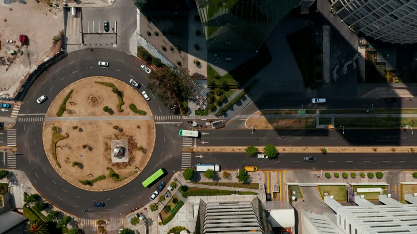 Top down view of a roundabout in the Santa Fe business district of Mexico City with cars and buses tracked by hexagon tags and speed labels, smart city traffic analytics HUD overlay, slow ascent