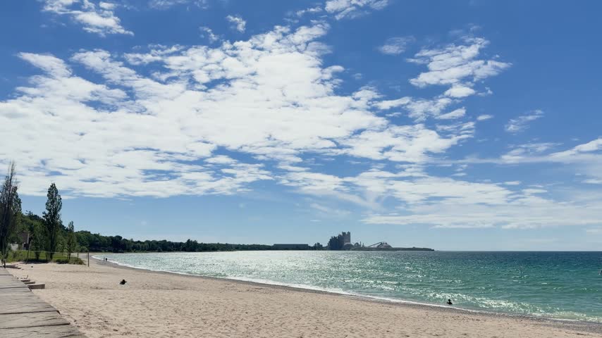 Scenic Lake Michigan sandy beach in Charlevoix, Michigan, with blue sky, scattered white clouds and sparkling lake water on a sunny summer day. 4K landscape footage.