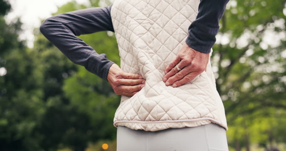 Senior, person and hands with back pain in park for outdoor injury, mistake or muscle tension. Elderly, woman and sore spine with ache or discomfort for overworked strain, workout accident or posture