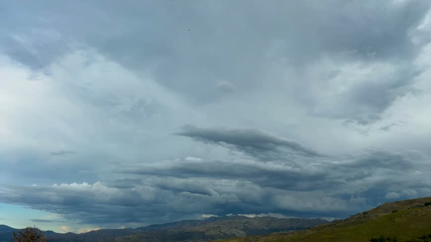 a layered shelf cloud formation and heavy overcast skies sweeping directly over a scenic mountain range before a storm.