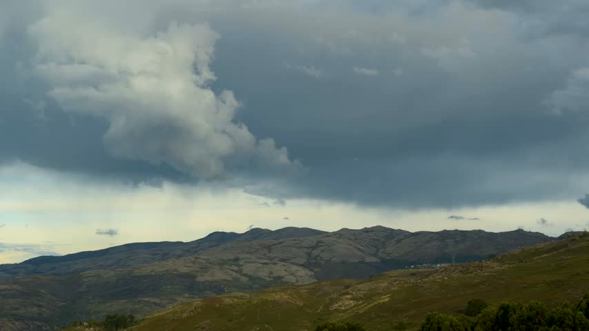 A cinematic wide shot capturing heavy dark storm clouds looming low and moving over a rolling rocky mountain landscape.