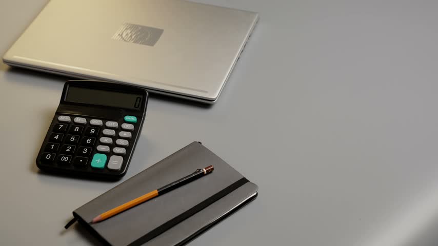 A laptop sits on a gray desk alongside a notebook and a calculator. The workspace is ready for productivity and business tasks throughout the day.