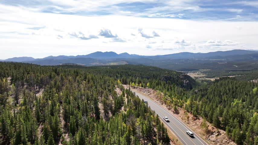 Breathtaking view of the Peak to Peak Highway in Colorado, inviting travelers to a scenic road trip adventure through the Rocky Mountains. Drone shot showing surrounding peaks.