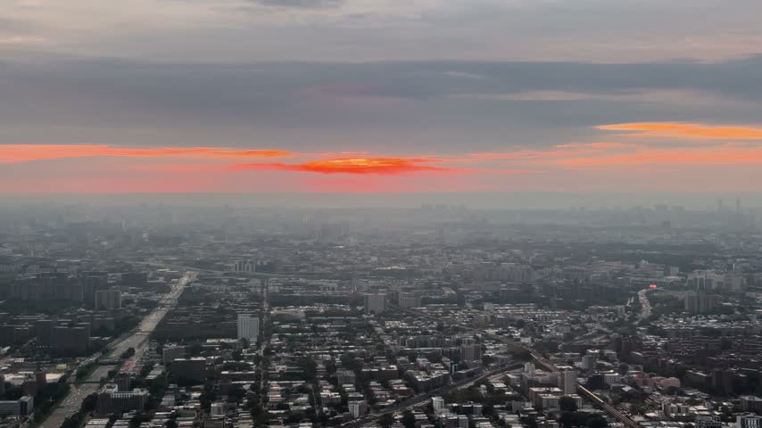 Aerial view over New York City at dusk with dramatic orange sunset clouds above skyline