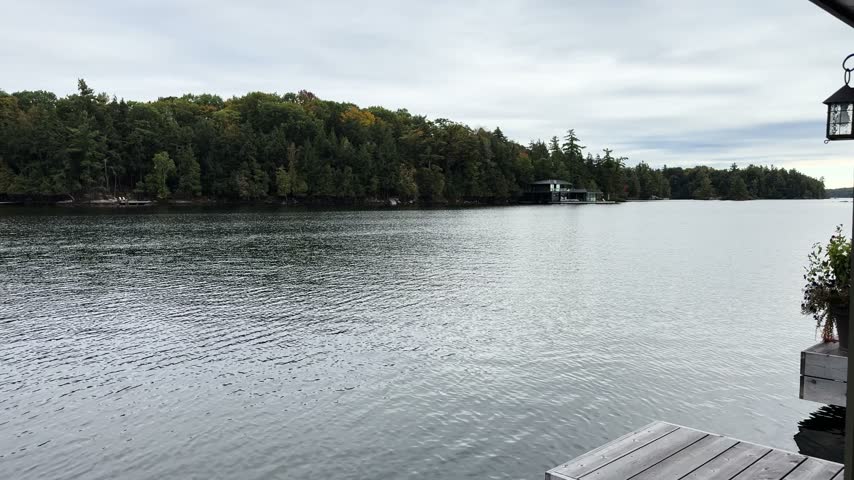 Calm lake water and forested shoreline under cloudy sky, viewed from a wooden dock