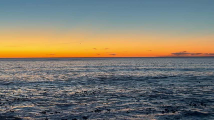 Orange sunset sky over calm rippling ocean with distant horizon