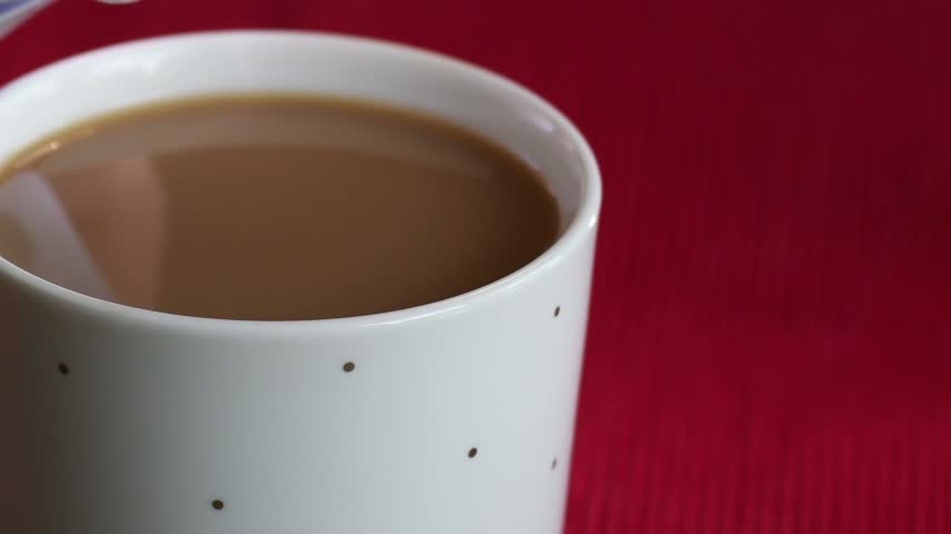 Pouring cream into a cup of coffee on a red background creates a cozy morning atmosphere