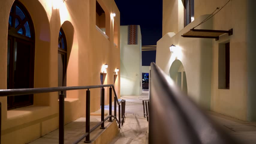 Slow camera movement exploring a beautiful illuminated alleyway in an old arabian town, showcasing traditional middle eastern architecture and narrow streets under a clear night sky