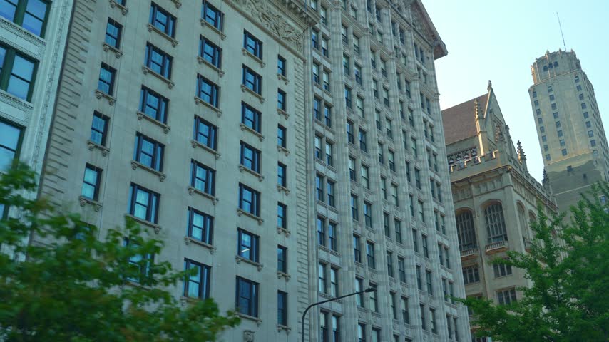 Tall historic Chicago buildings with detailed stone facades and windows rise into a clear blue sky. Urban architecture and high-rise structures create a classic downtown skyline view.