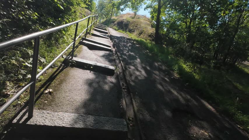 POV walking up stone stairs on a hiking trail in a green sunny park