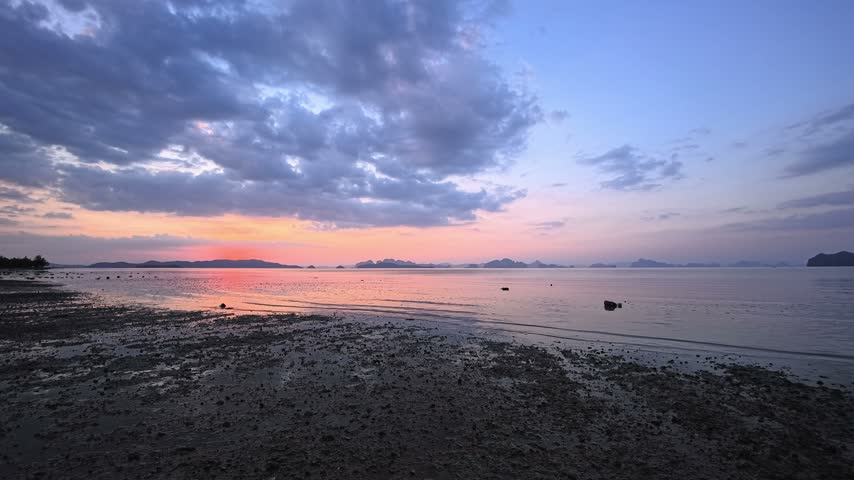 Tropical beach at sunset on Koh Yao Noi, a paradise island in Thailand, with limestone karsts in Phang Nga Bay. This sandy beach in Southeast Asia has pink and orange sunset reflections on the sea. Tropical sunset over an island paradise, with a colorful sky and distant islands on the horizon. The beach is exposed at low tide, with wet sand along the tropical coast. A sunset seascape on this Thai island.