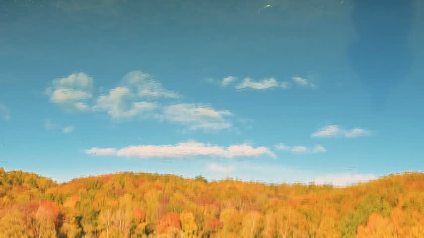 An autumn landscape reflected in a lake, featuring trees in vibrant autumn colors against a clear blue sky.