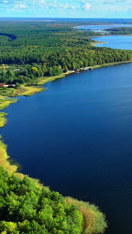 Aerial view of serene blue lake surrounded by dense green forests and clear skies with clouds