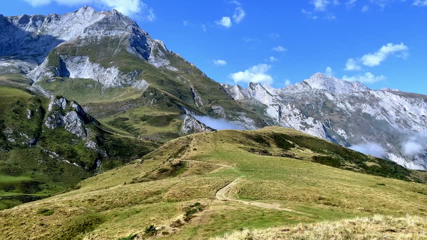 scenic mountain trail on green ridge leading towards rocky alpine peaks under blue sky in French alps
