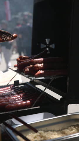 Delicious hot dogs grilling on a barbecue at an outdoor street food fair on a sunny summer day