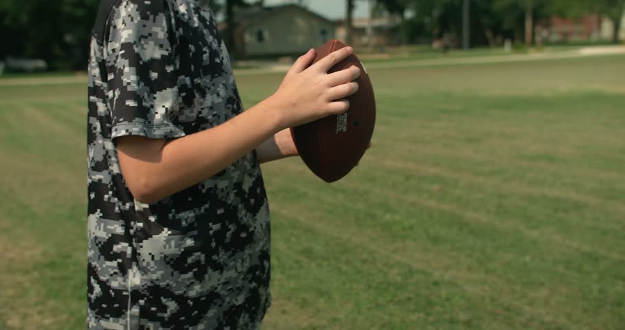 Close view of a young boy gripping and throwing an American football while playing on a grassy field.