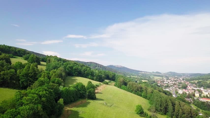 Aerial view descending toward the town of Jeseník with apartment blocks and industrial buildings in the valley beneath the forested Jeseníky Mountains, Czech Republic.