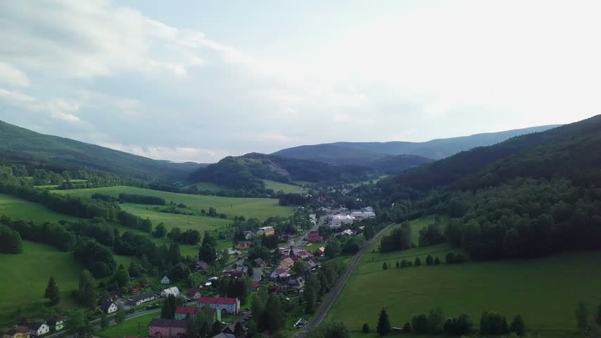 Aerial view of red-roofed houses in the valley of Horní Lipová surrounded by meadows, spruce and deciduous forest slopes and mountain ridges, Jeseníky, Czech Republic.