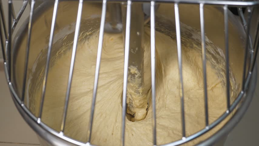 Industrial electric spiral kneading machine for kneading bread dough. Dough for pizza or bread is kneaded in the machine. Camera shoots from above through metal grille.