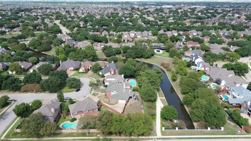Orderly waterfront homesites border through Waterways neighborhoods, revealing residential rooftops along Valley Ranch Greenbelt. Lush greenbelts border flowing blue channels, Irving, Texas. USA.