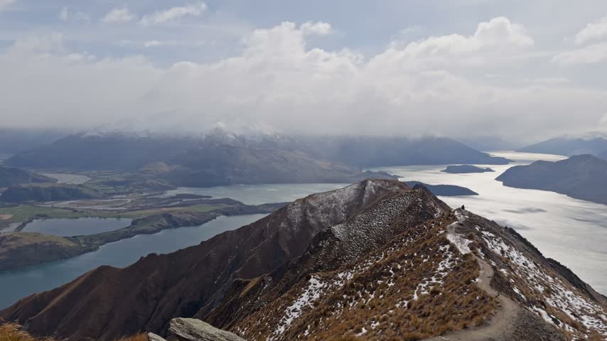Scenic mountain ridge trail overlooking lakes and valleys under dramatic cloudy sky