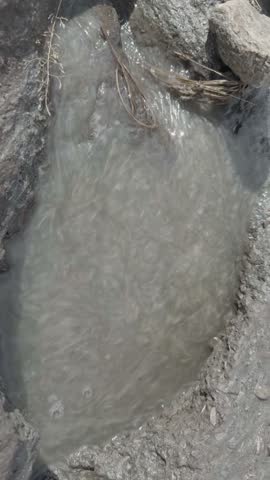 Muddy water streams into a shallow depression in rocky soil, rural outdoor setting