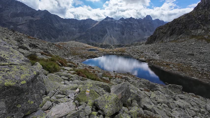 Rocky Alpine Hiking Trail Overlooking Mountain Tarn and Rugged Peaks