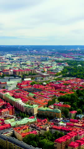 Vertical video. Gothenburg, Sweden. A sweeping aerial panorama captures the historic city center with its dense grid of characteristic red-tiled rooftops and stone buildings stretching toward the Gota Alv river. The camera glides smoothly over the urban fabric, revealing the river