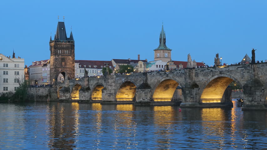 The Charles Bridge on Vltava River at dusk in city of Prague, Czech Republic. Medieval stone bridge with illuminated arches in the evening.