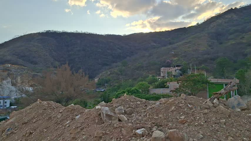 Scenic landscape of rural hills and construction site with earth mound under a partly cloudy sky.