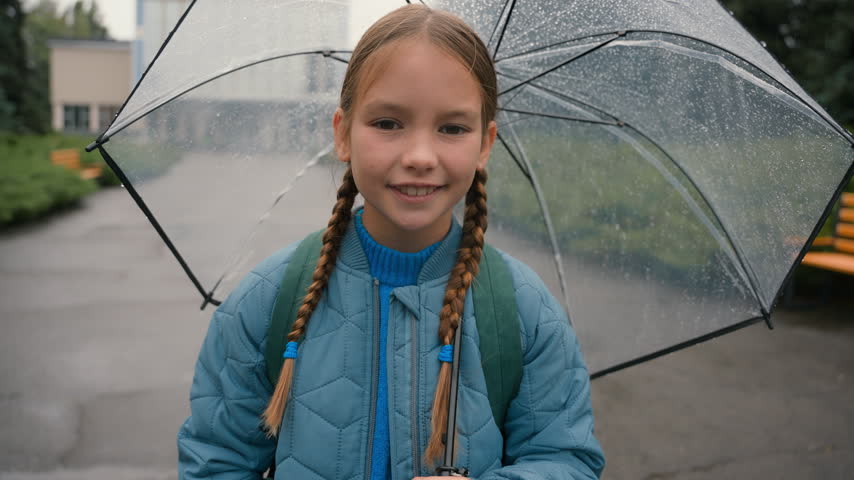 Portrait happy healthy Caucasian little school girl looking at camera smiling toothy holding umbrella at city rain weather cheerful daughter child learner kid pupil smile good mood enjoying raining