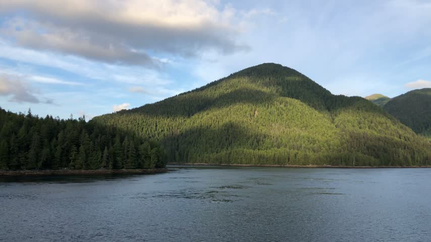 Sunlit evergreen hills above a calm coastal inlet in British Columbia, Canada.