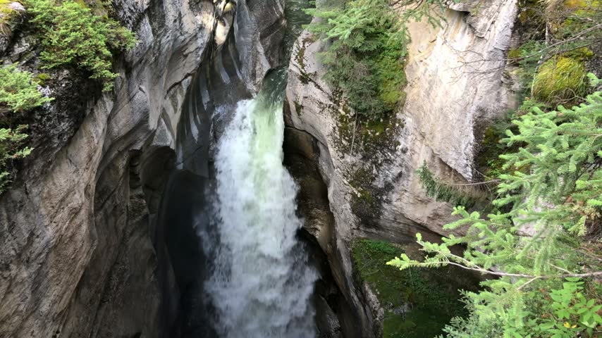 Waterfall dropping into a deep wooded canyon in western Canada.