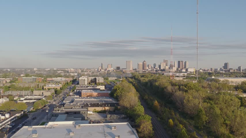 Drone aerial of natural forest fire near urban downtown center of Columbus Ohio as smoky flames and dark black smoke rise near wooded forested area from burning garbage by car highway and city traffic