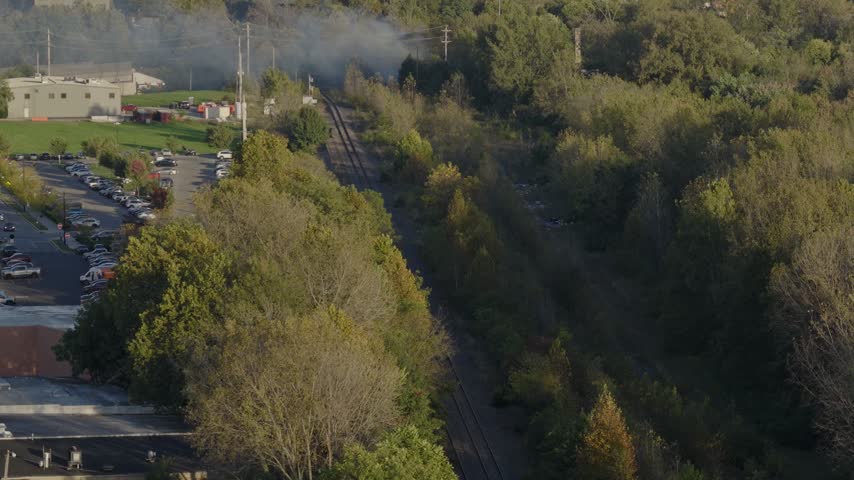 Drone aerial of natural forest fire near urban downtown center of Columbus Ohio as smoky flames and dark black smoke rise near wooded forested area from burning garbage by car highway and city traffic