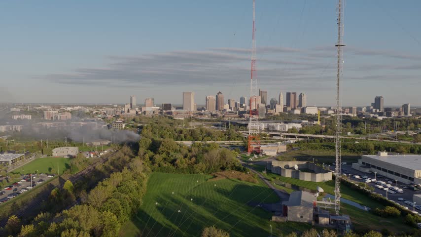 Drone aerial of dark clouds of smoke rising from small forest fire outside city downtown center of Columbus, OH as flames create smoky air conditions by Ohio capital near i315 highway and car traffic