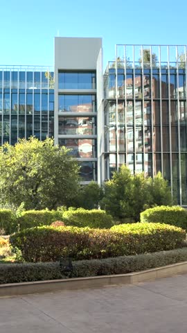 A contemporary glass building surrounded by lush greenery and manicured hedges in the Community of Madrid, showcasing urban architecture and natural landscaping.