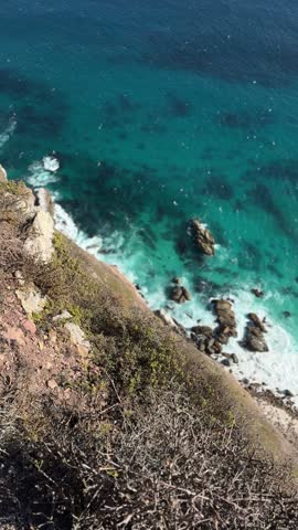 Aerial view from a coastal cliff overlooking crystal clear turquoise ocean water, rocky shoreline and waves at the Cape of Good Hope, Cape Town, South Africa.