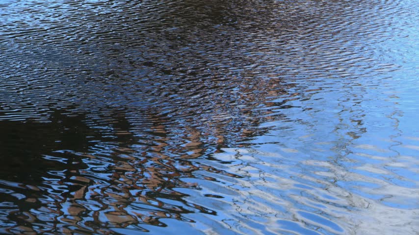 Blue water surface with gentle ripples and reflections of light and surrounding objects at the Millstone Aqueduct in New Jersey, USA, which carries the Delaware and Raritan Canal over the Millstone River.