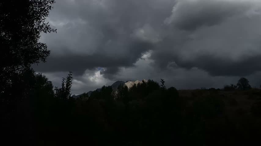 Dark storm clouds moving over mountain peak with silhouetted trees