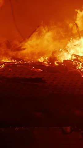 A large fire engulfs the building, with flames towering into the air. The intense fire produces smoke and an ominous glow, affecting the surrounding area.