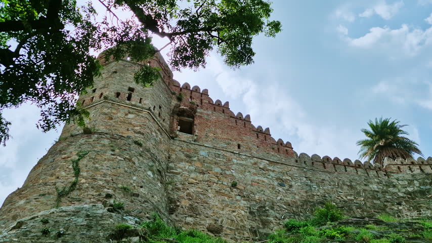 A rounded stone bastion and crenellated wall rise beneath trees at Kumbhalgarh Fort on an Udaipur trip.