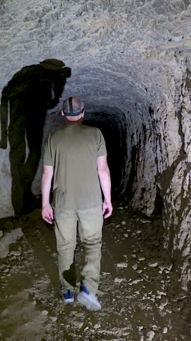 Person from behind walking through a dark rocky cave tunnel with a headlamp going deep into darkness concept of exploration and unknown.