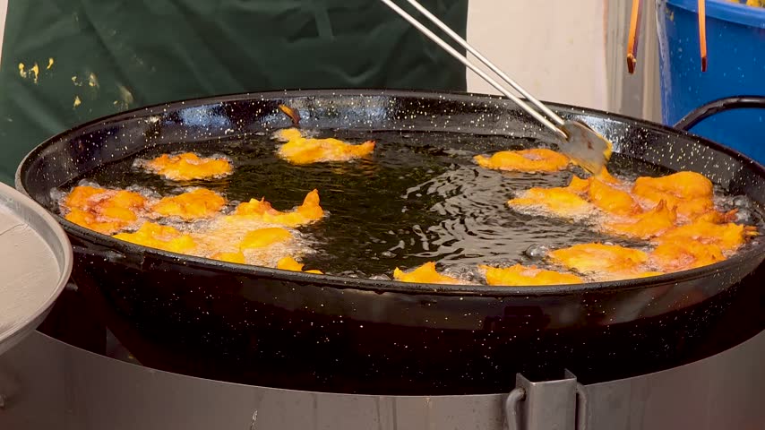 Traditional Spanish bunuelos frying in hot boiling oil in a large pan at a street food festival market.