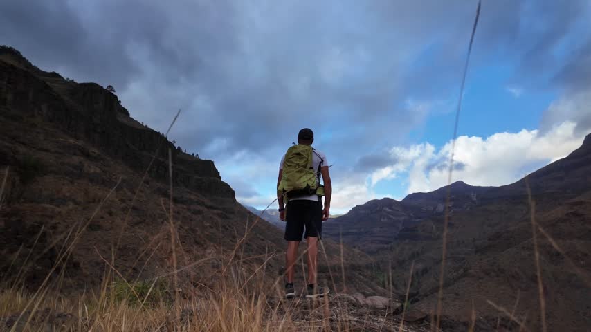 Young man hiker with a backpack standing on top of a mountain with his arms raised, expressing feelings of freedom, success, and connection with nature in a beautiful arid landscape