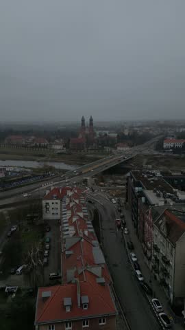 Aerial footage moves toward a historic twin tower church as traffic crosses a bridge over the river in a foggy European city