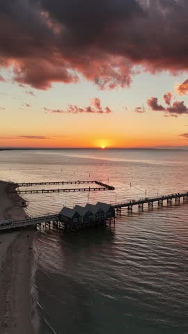 Aerial view along Busselton Jetty with the sun low over the water, Western Australia. Timber piles cast long shadows on the shallows. A landmark of Western Australia