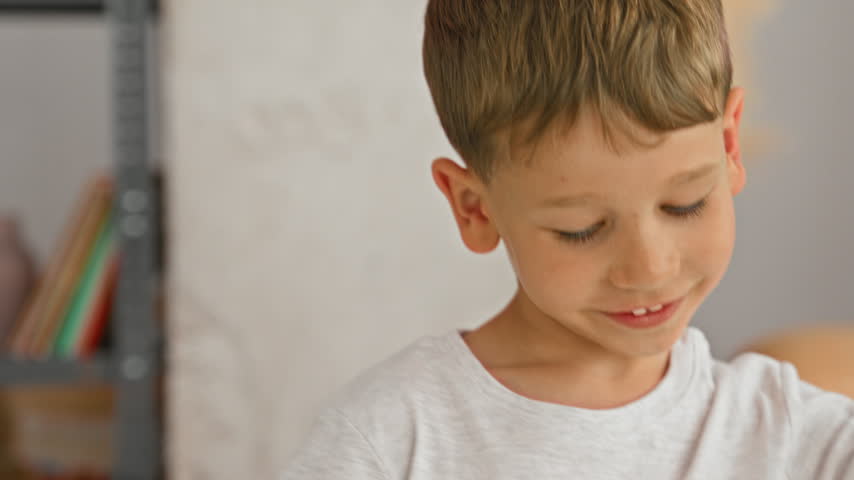 Boy holds soft pillow with one hand and looks down while seated on a bed in building; quiet contemplation.