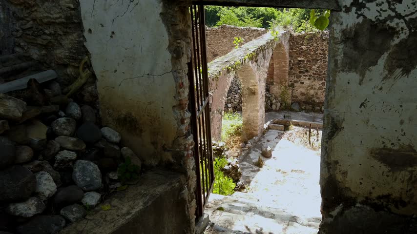 Ground level view of weathered stone ruins with arched passageways and overgrown walls surrounding an old courtyard at a historic site in Mexico under bright daylight.